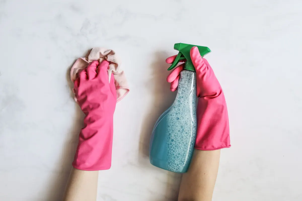 Gloved hands cleaning a surface with a cloth and spray